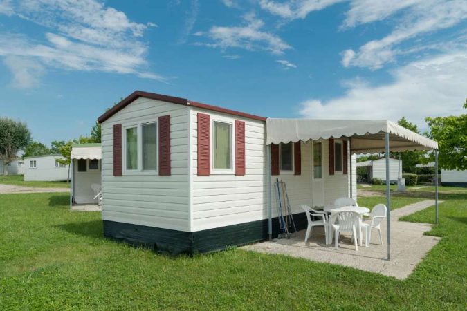 Mobil-home d'occasion blanc avec volets rouges et terrasse couverte dans camping verdoyant