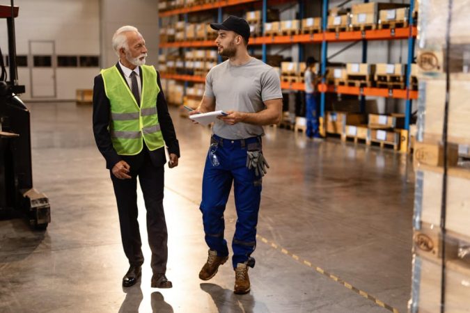 Deux professionnels discutant dans un entrepôt industriel avec des étagères de stockage en arrière-plan