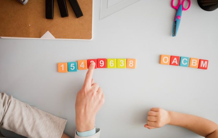 Des mains d'adulte et d'enfant manipulent des tuiles numérotées et lettrées, illustrant la manière de découvrir les mathématiques ludique avec le coffret Montessori