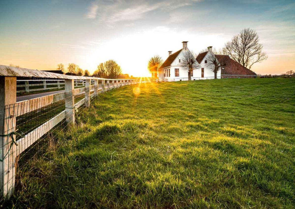 Une maison de ferme traditionnelle au coucher du soleil, avec une clôture et un champ.