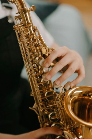 Main d'enfant sur les clefs d'un saxophone, détaillant un instrument à vent pour enfant.