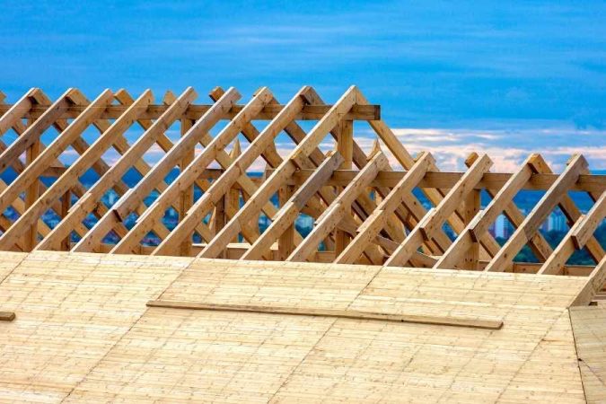 Fermes de charpente en bois alignées sur un toit en construction sous un ciel bleu