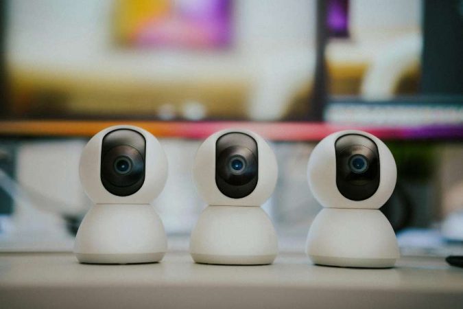 Trois caméras de surveillance connectées blanches avec rotation panoramique posées sur un bureau