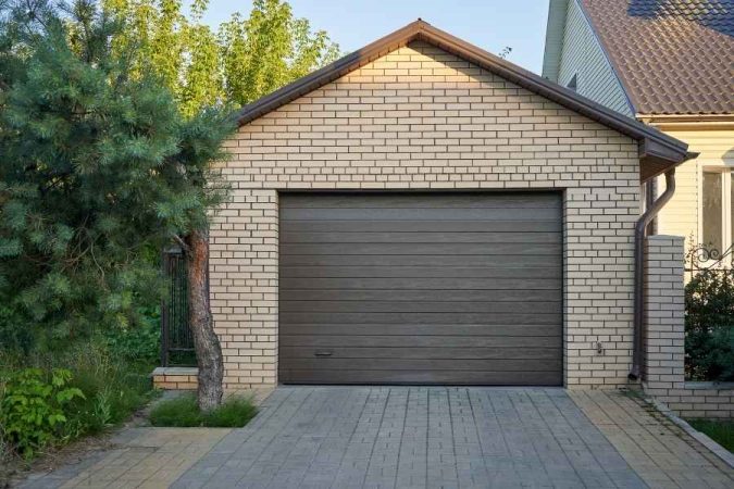 Garage indépendant en briques beiges avec porte sectionnelle grise et allée pavée