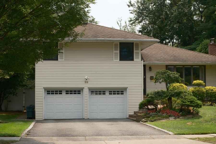 Garage intégré à la maison idéal pour un projet d’aménagement Maison avec garage double intégré et portes blanches sous bardage beige