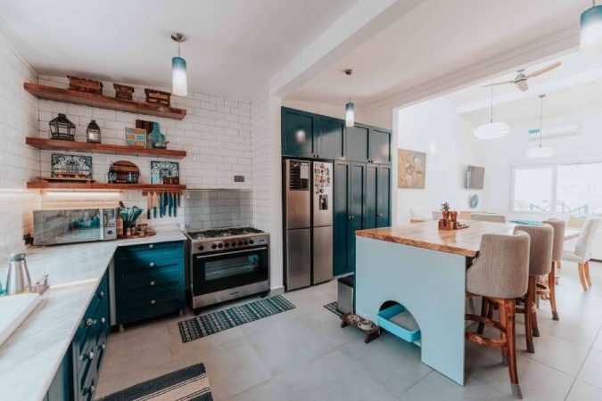 Cuisine ouverte style industriel doux avec meubles bleu canard, étagères en bois et carrelage métro blanc