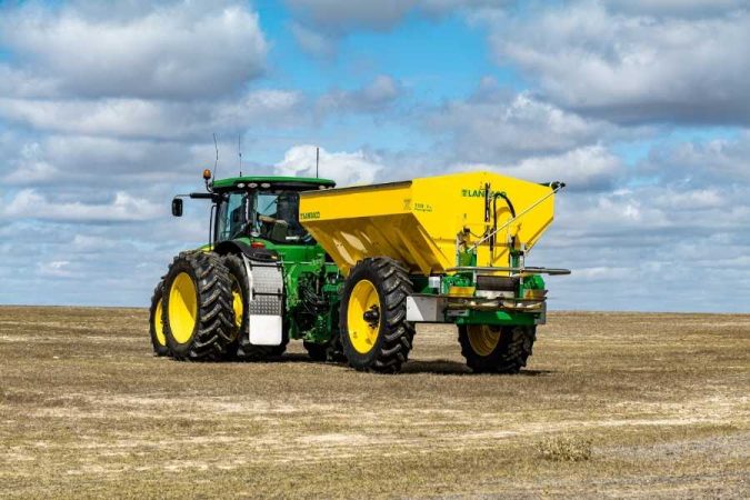 Tracteur agricole moderne avec épandeur jaune sur des terres agricoles ouvertes