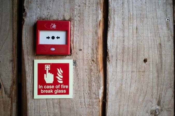 Déclencheur manuel d'alarme filaire incendie rouge installé sur mur en bois avec panneau d'instructions