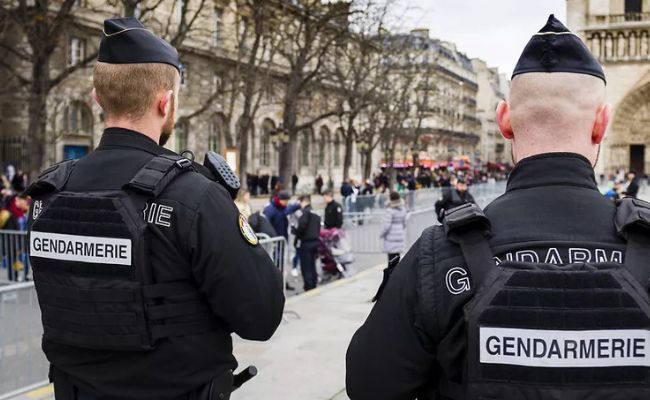 Deux gendarmes en tenue d'intervention, vus de dos, portant des gilets tactiques et des képis.