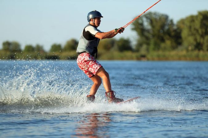 Jeune homme pratiquant le wakeboard tiré par un bateau ou un câble sur un plan d'eau.