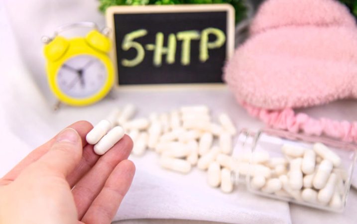 Gélules de Griffonia posées sur une table à côté d'un réveil et d'un masque de sommeil.