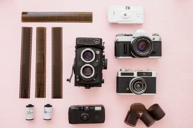 Collection d'appareils photo argentiques vintage et de pellicules 35mm sur fond rose, illustrant l'univers de la photographie avec Fujifilm Maroc.