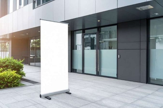 Un grand roll up personnalisé blanc et vierge installé devant l'entrée moderne d'un bâtiment d'entreprise.