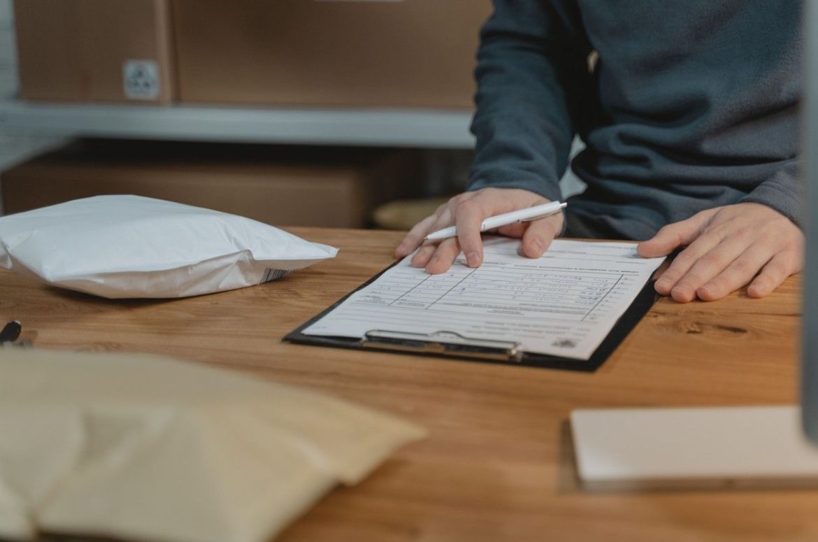 Une personne remplit un formulaire officiel sur une table en bois entourée de colis, illustrant les démarches administratives de déménagement.