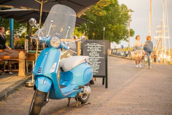 Un scooter bleu élégant équipé d'un déflecteur de bulle transparent est garé le long d'une rue pavée.