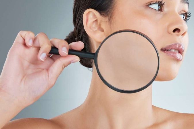 Une femme examine sa joue avec une loupe pour sublimer sa peau après 40 ans.