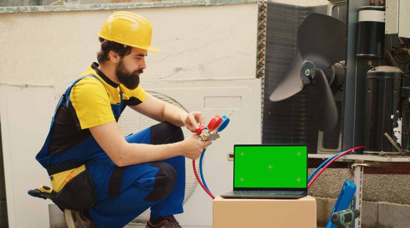 Un technicien en gilet et casque de chantier effectue un diagnostic face à un ordinateur portable pour résoudre une fuite d eau circuit de chauffage encastré.