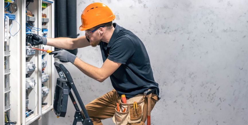 Un électricien avec casque orange intervient sur un tableau lors d'une rénovation électrique de maison ancienne.